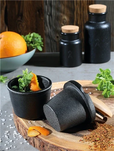 Black ceramic spice grater containers on a wooden board with herbs and spices