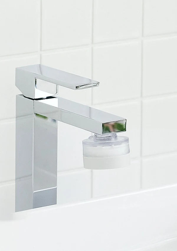 A modern chrome single-handle bathroom faucet with a clear cylindrical filter attachment, mounted against a white tiled wall.