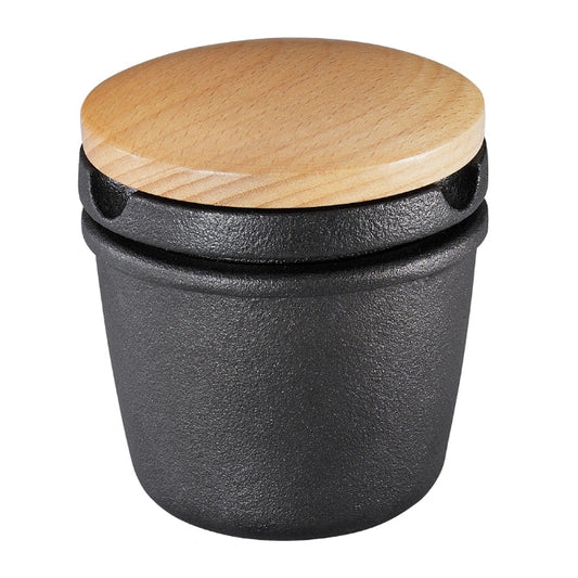 Black cast iron spice grater with a wooden lid on a white background