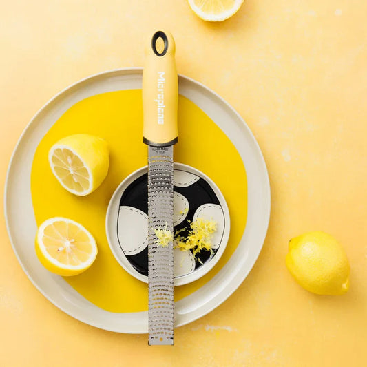Zester with a yellow handle on a plate with lemons against a yellow background