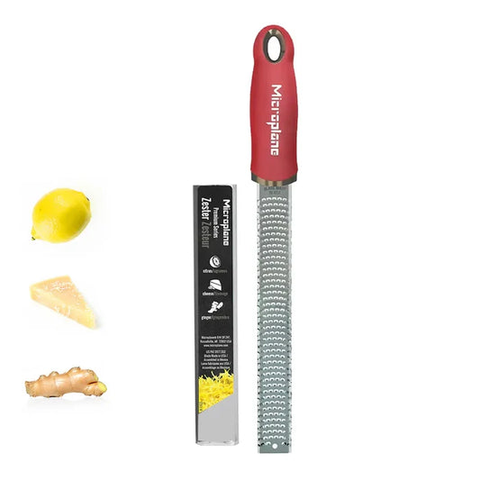 Red microplane zester with a lemon, cheese, and ginger on a white background