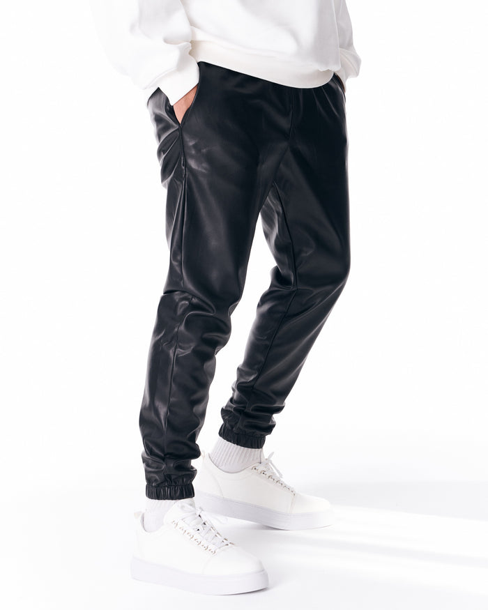 Martin Valen oversized leather jogger in black, three-quarter view showing elastic waist, gathered cuff and white sneakers