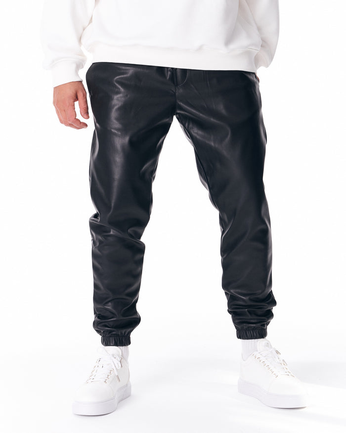 Martin Valen oversized leather jogger in black, three-quarter view showing creased legs, elastic cuffs and white sneakers