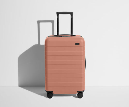 Front product view of The Bigger Carry-On suitcase in Clay Pink with raised handle